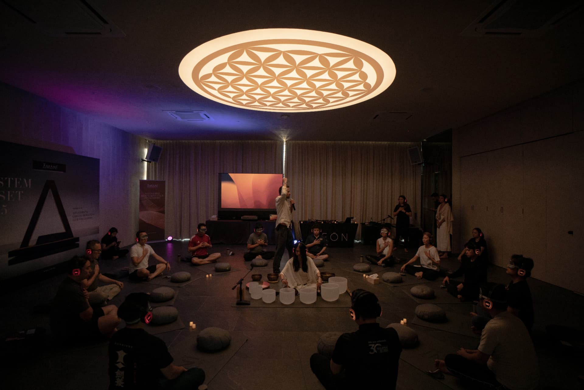 Participants seated in a sound healing circle under a flower-of-life light at the System Reset Experience